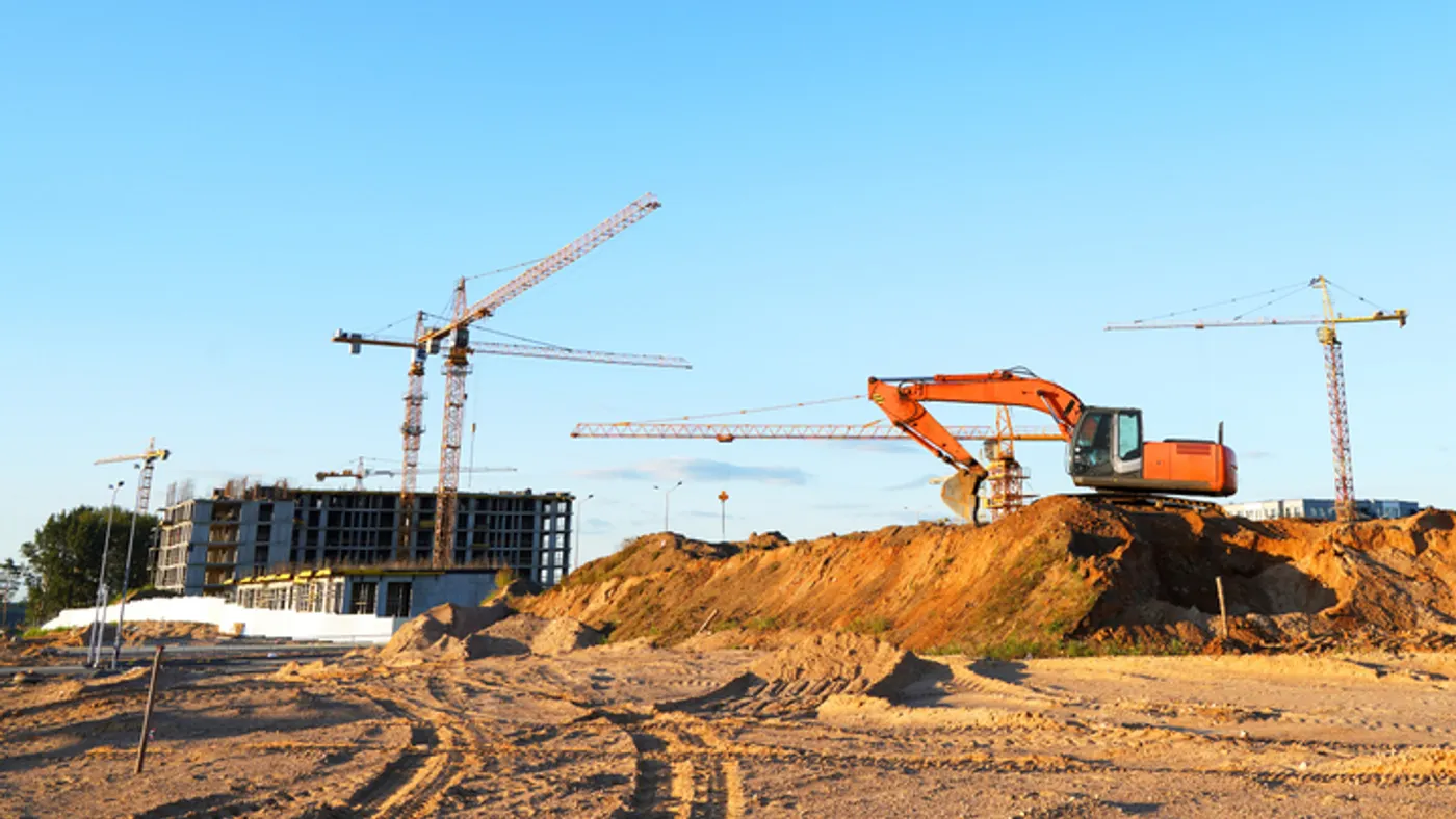 Large cranes tower over dirt and construction machinery on a jobsite.