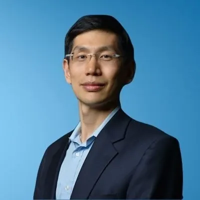 A headshot of a person wearing glasses with a blue background