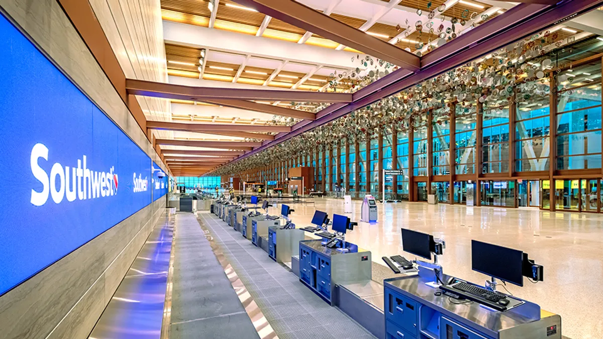 Interior of terminal shows new check in kiosks with a spacious glass wall in the background with exposed beams and art hanging from the ceiling.