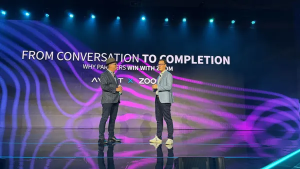 two men standing on stage behind a slide that says "From conversation to completion"