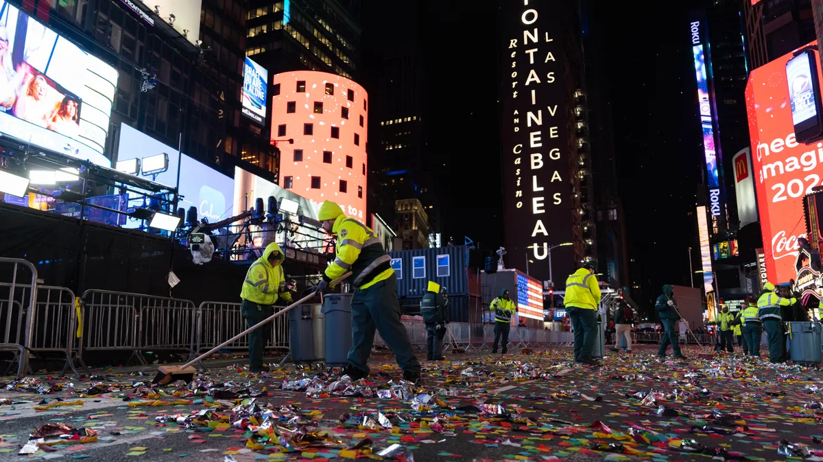 A person sweeps up confetti in Times Square, where an ad for Fontainebleau is visible on a building behind them.