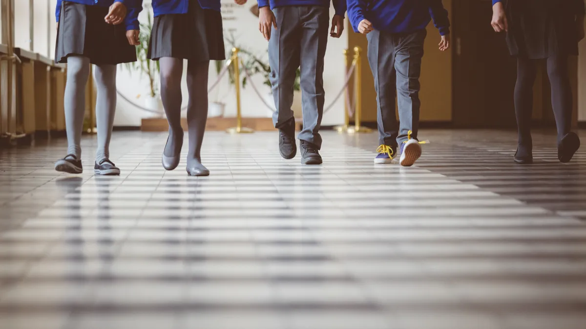 Photo of students, pictured from waist down walking down a school hallway. They are dressed in school uniform clothes.