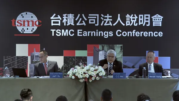 Three men in business suits sitting at a table facing an audience, TSMC logo in background.