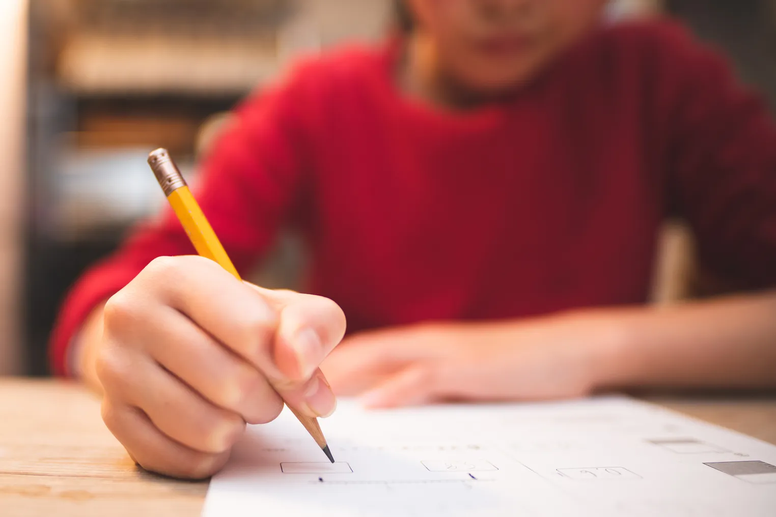 Camera has close-up of pencil being held by person sitting at a desk