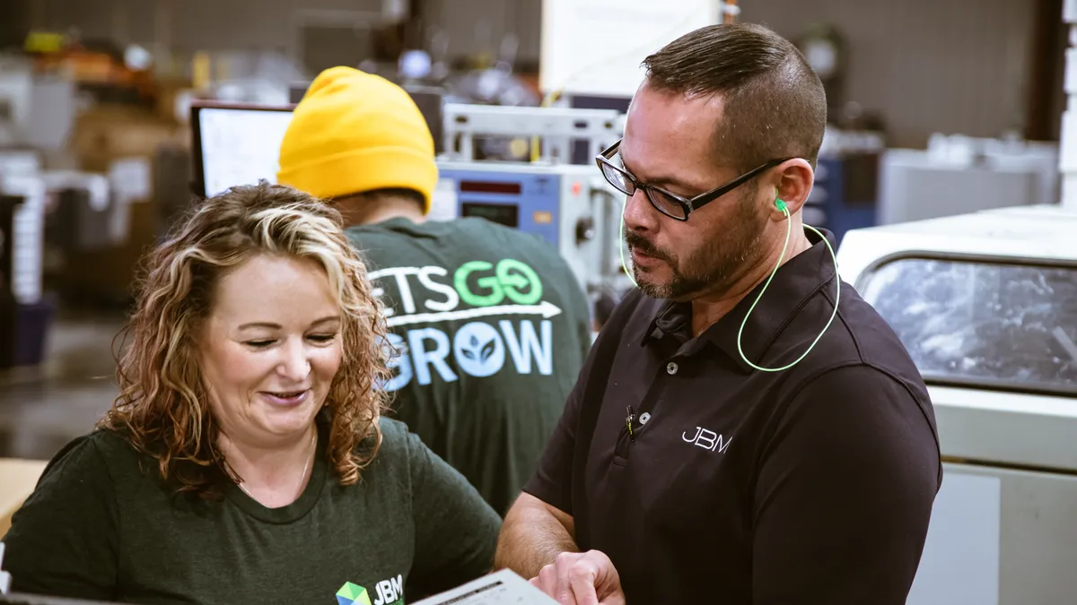 Two people reading a document in an industrial workplace setting.