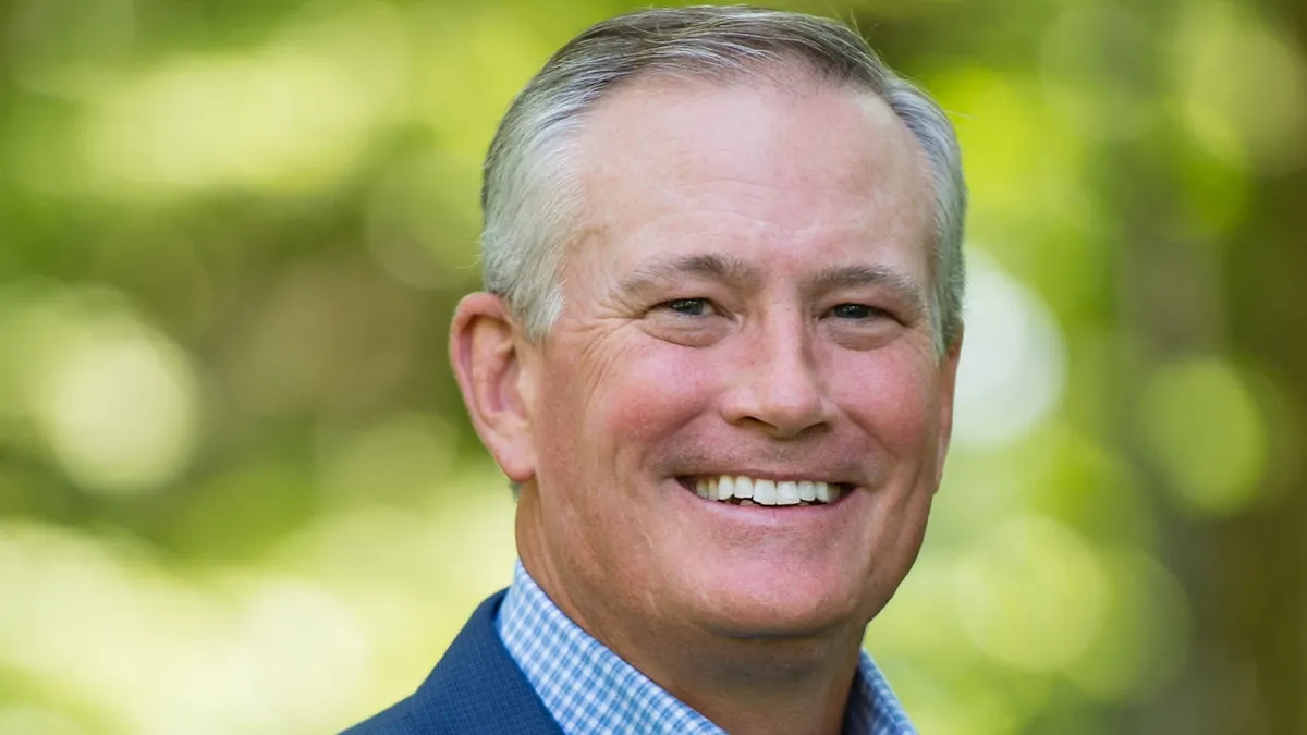 Brian Blaser is smiling in a headshot with a blurred deep green background.