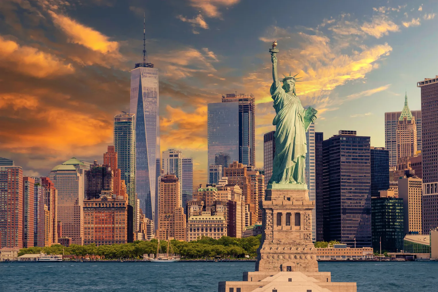 Statue of Liberty and New York City Skyline with Manhattan Financial District, Battery Park, Water of New York Harbor, World Trade Center, Sail Boat and Dramatic Orange and Blue Sunset Sky with Clouds