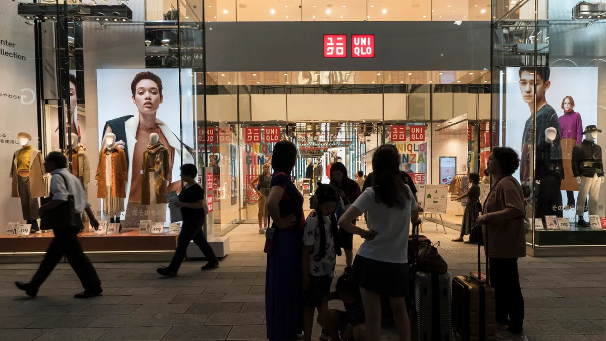 A view of the exterior of a Uniqlo store, where people walk past it and wait in front of it.