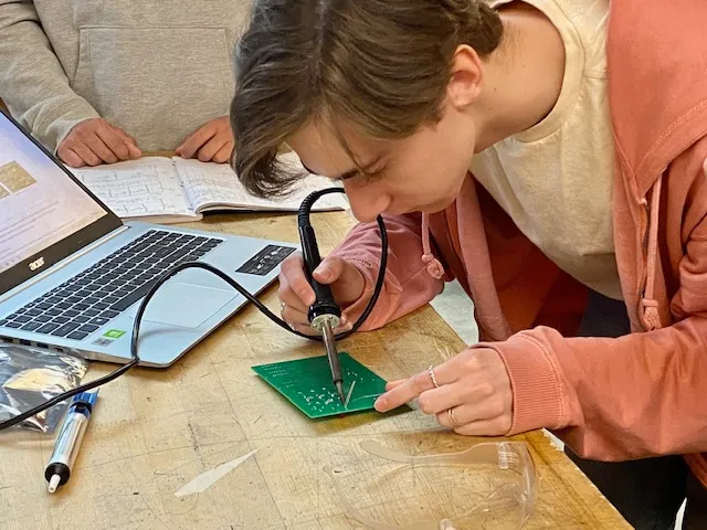 High School student builds a circuit board in a classroom.