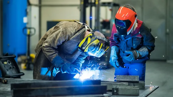 Blonde woman works as a welder in workshop, operating welding machine, wearing protective clothing and a welding mask