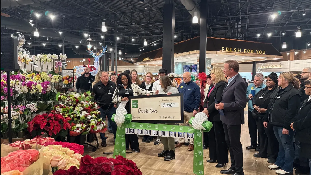 Group of people presenting a large check in teh floral section of a grocery store