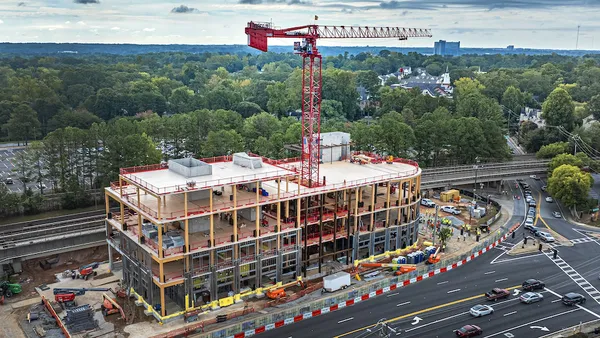 An aerial view of a building under construction. The jobsite is cordoned off, and a crane rises through the middle of the structure.