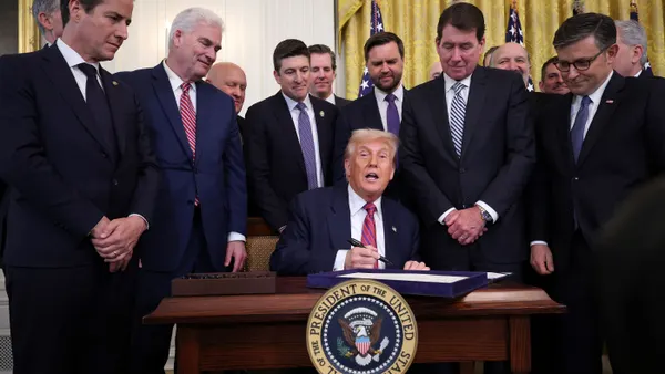 President Donald Trump sits at desk with pen in hand.