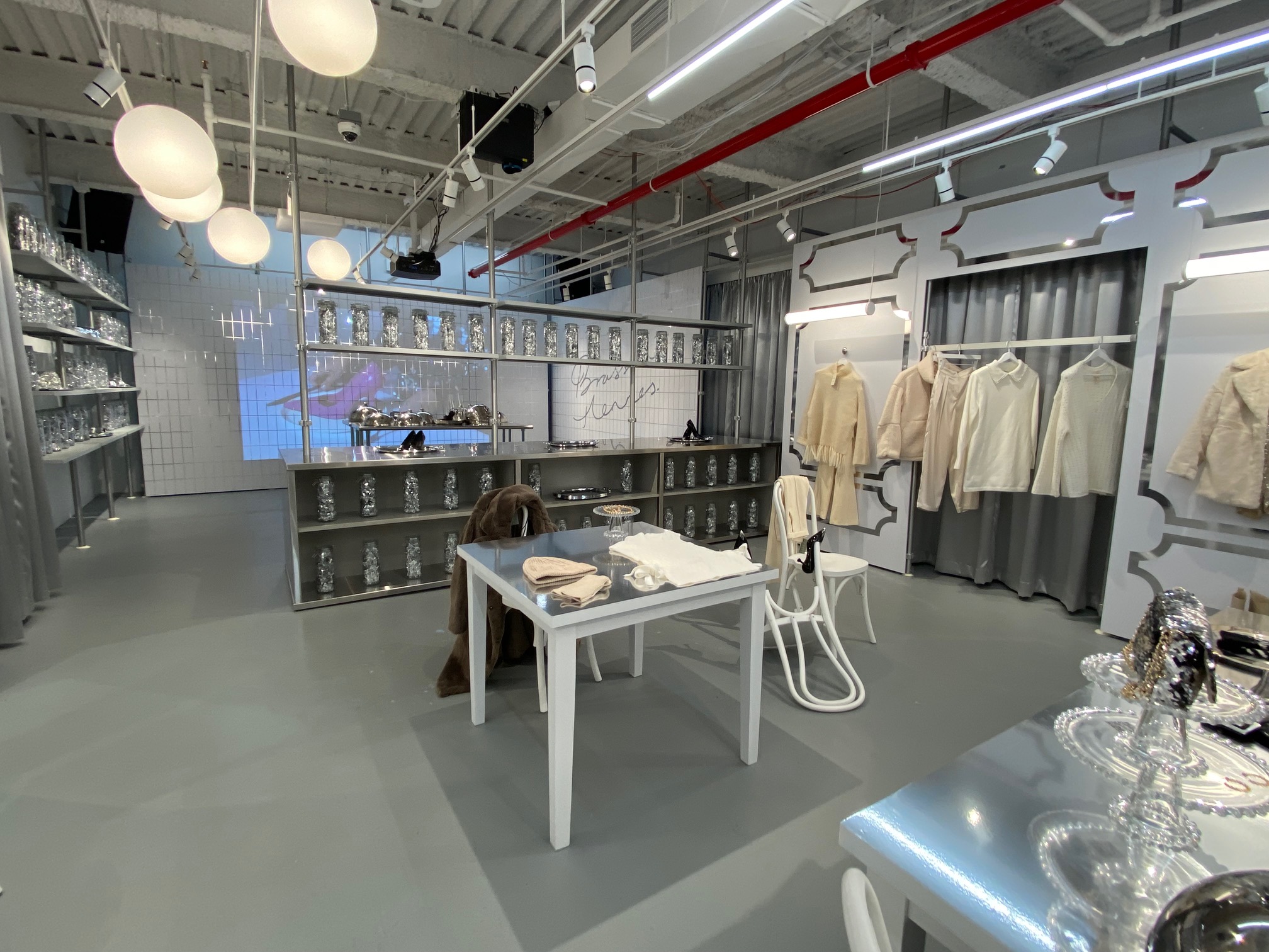 A room with a center table with merchandised clothes. Shelves with silver tinsel line a wall on the left.