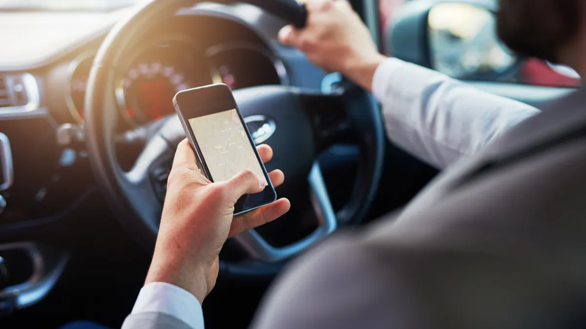 Closeup of man holding a smartphone showing driving directions in his left hand while his right hand is on the steering wheel.