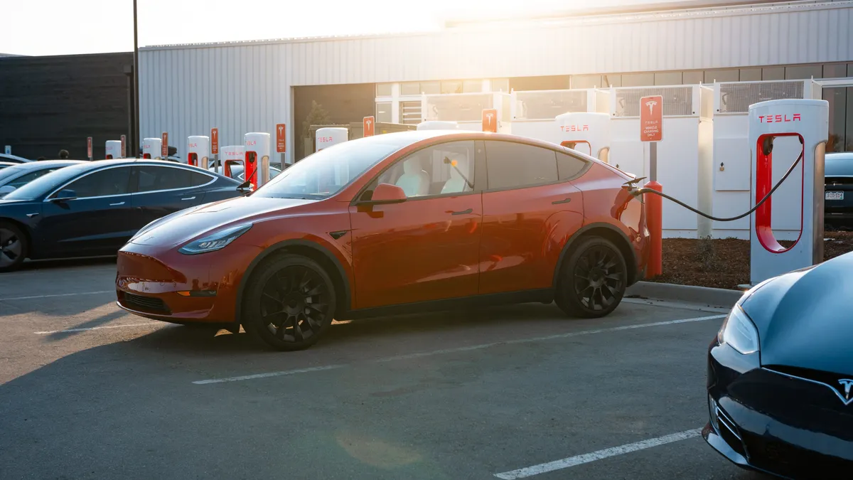 A red Tesla Model Y plugged in for charging at a Tesla Supercharger station.