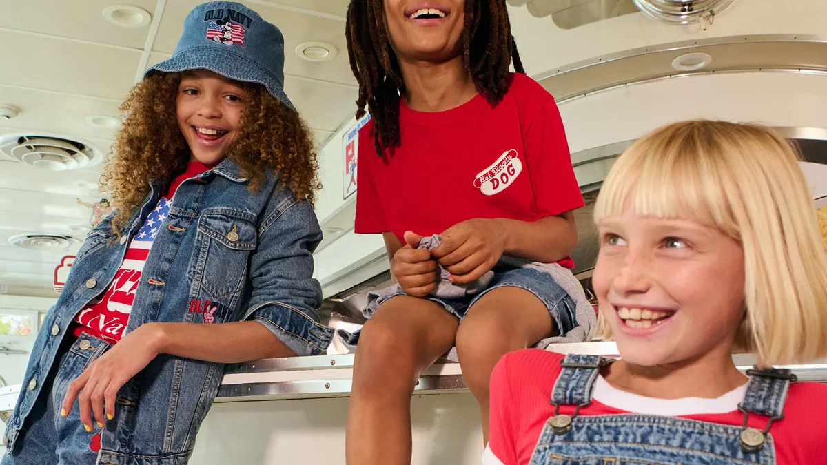 Three children sit together laughing wearing clothes from the Old Navy and Disney collection.