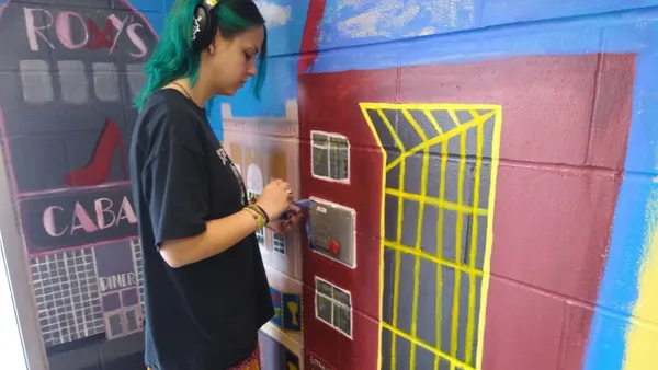 A student paints a mural on a wall with bright colors