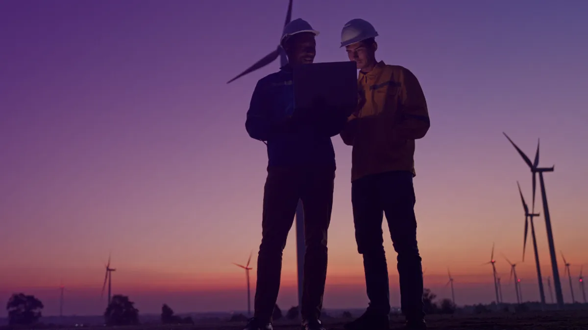 Silhouette shot of two electrical engineers standing in front of wind turbines