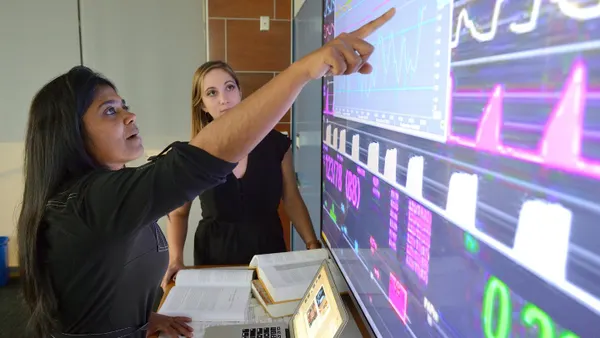 A person points to a large screen showing vital signs.