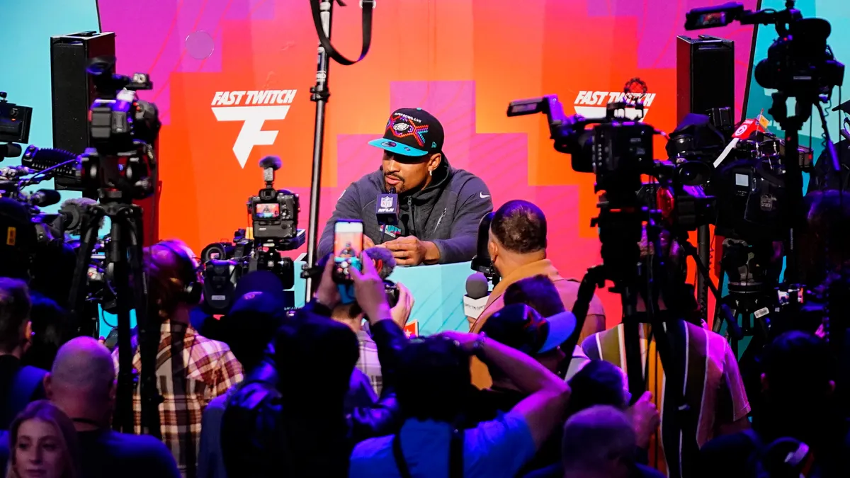 Person in hat surrounded by cameras at a press conference