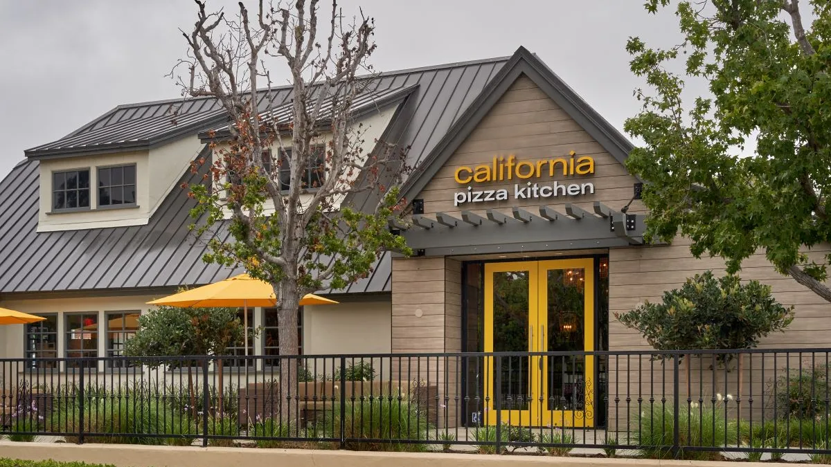 An image of a light brown building with a small tree out front that lost its leaves. The signage says California Pizza Kitchen.