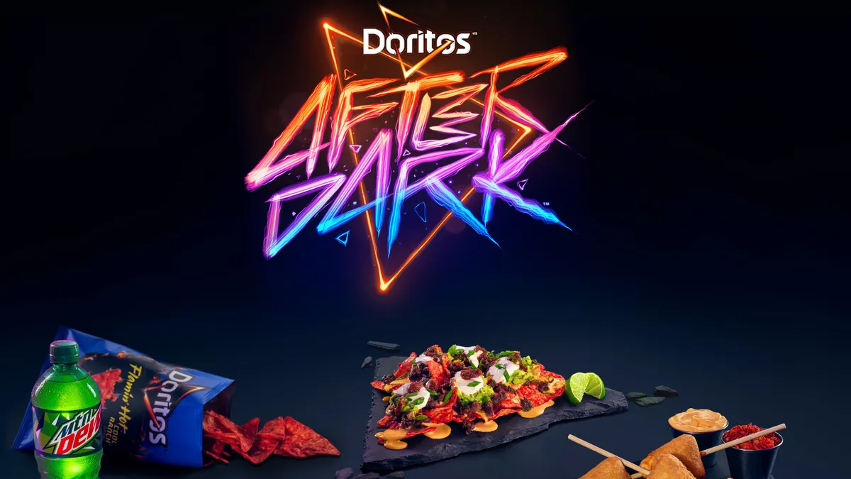 A turned over blue bag of Doritos and several dishes prepared with the chips sit under multi-colored neon branding reading, "Doritos After Dark."