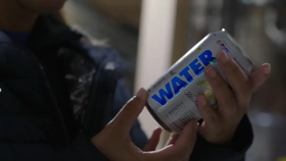 Someone holds a can of water against a blurred background.