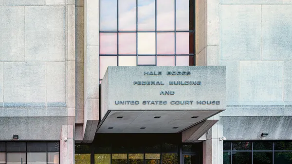 A gray, brutalist style building is seen up close with "Hale Boggs Federal Building and United States Court House" on a sign above glass doors.