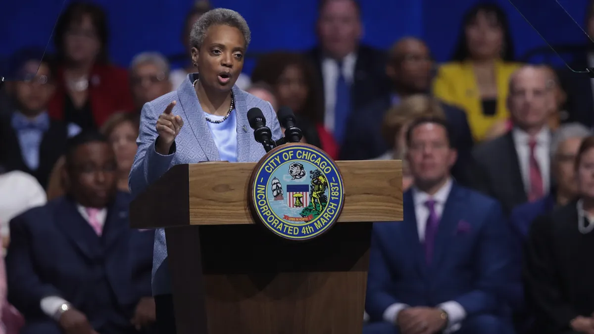 Mayor Lori Lightfoot stands at a podium in front of a crowd of people