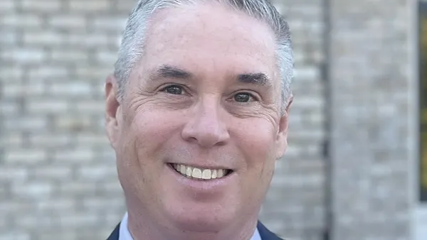 A person wearing a gray blue suit smiling