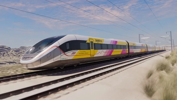 A white, gray, yellow and hot pink rail train on a track in the desert.