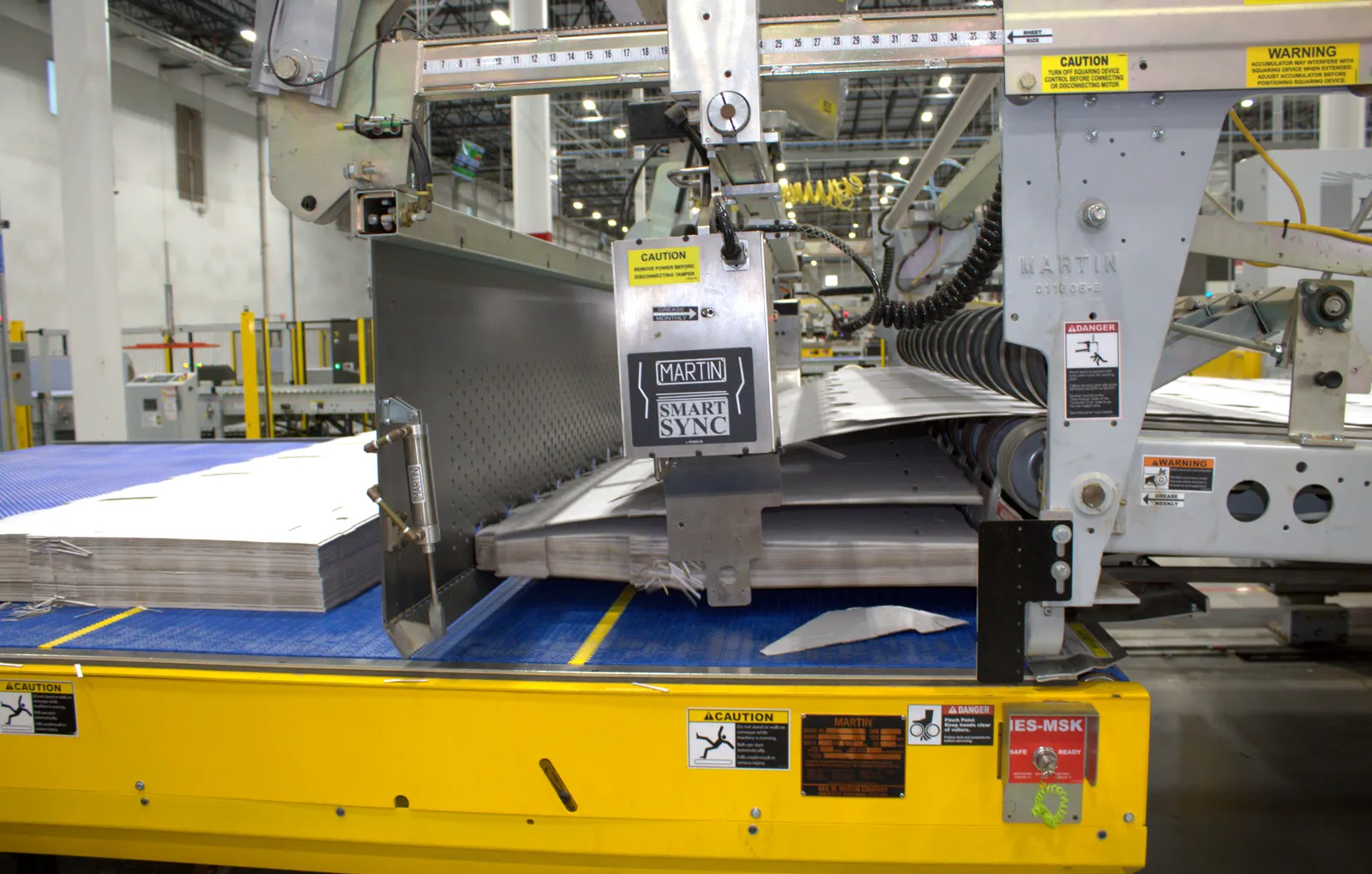 A close-up view of a piece of industrial equipment with stacks of flat corrugated boxes.