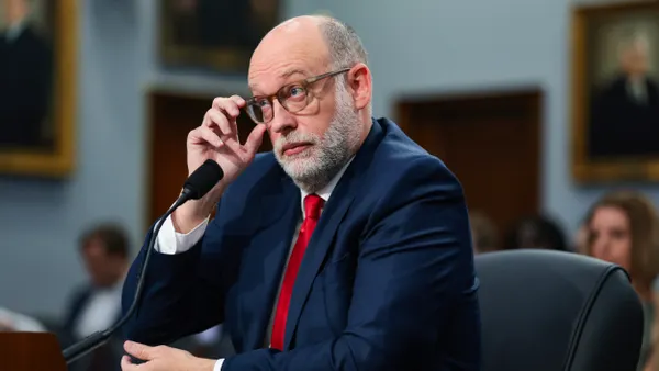 A person wearing a suit and red tie sitting at a table adjusts glasses.
