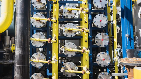 A close-up of several round metal discs ringed by bolts, most of which are hooked up to a tube, at an industrial facility.