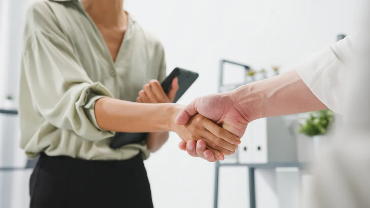 Multiracial group of young creative people in smart casual wear discussing business shaking hands together and smiling while standing in modern office. Partner cooperation, coworker teamwork concept.