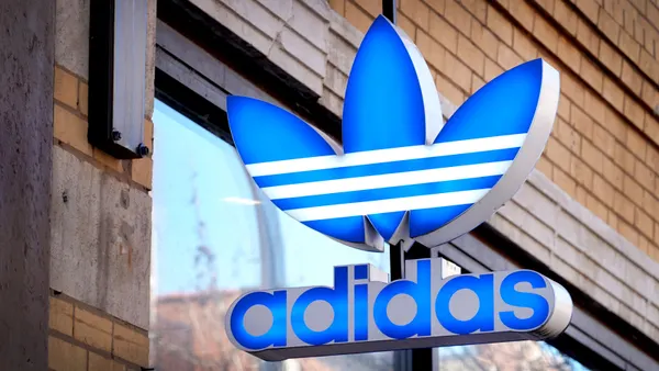 A closeup of a blue Adidas logo sign hanging outside a store.