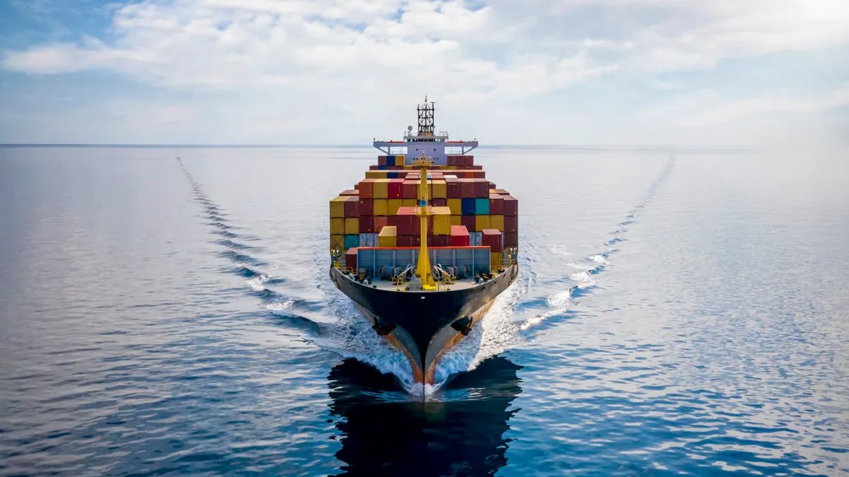 Aerial front view of a loaded container cargo vessel traveling over calm ocean