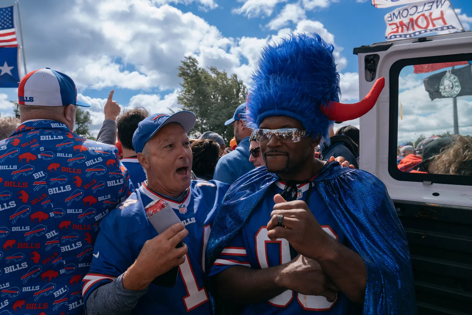 Anthony "Spice" Adams, wearing Buffalo Bills paraphernalia, stands next to a fan at a tailgate