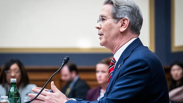 Scott Bessent, secretary of the Treasury Department, speaks into a microphone while gesturing with his hands, with blurred onlookers in the background.