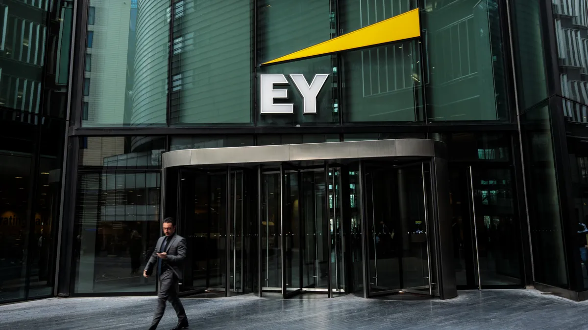 The photo shows a business person exiting an office building's door over which an Ernst & Young label is hung.