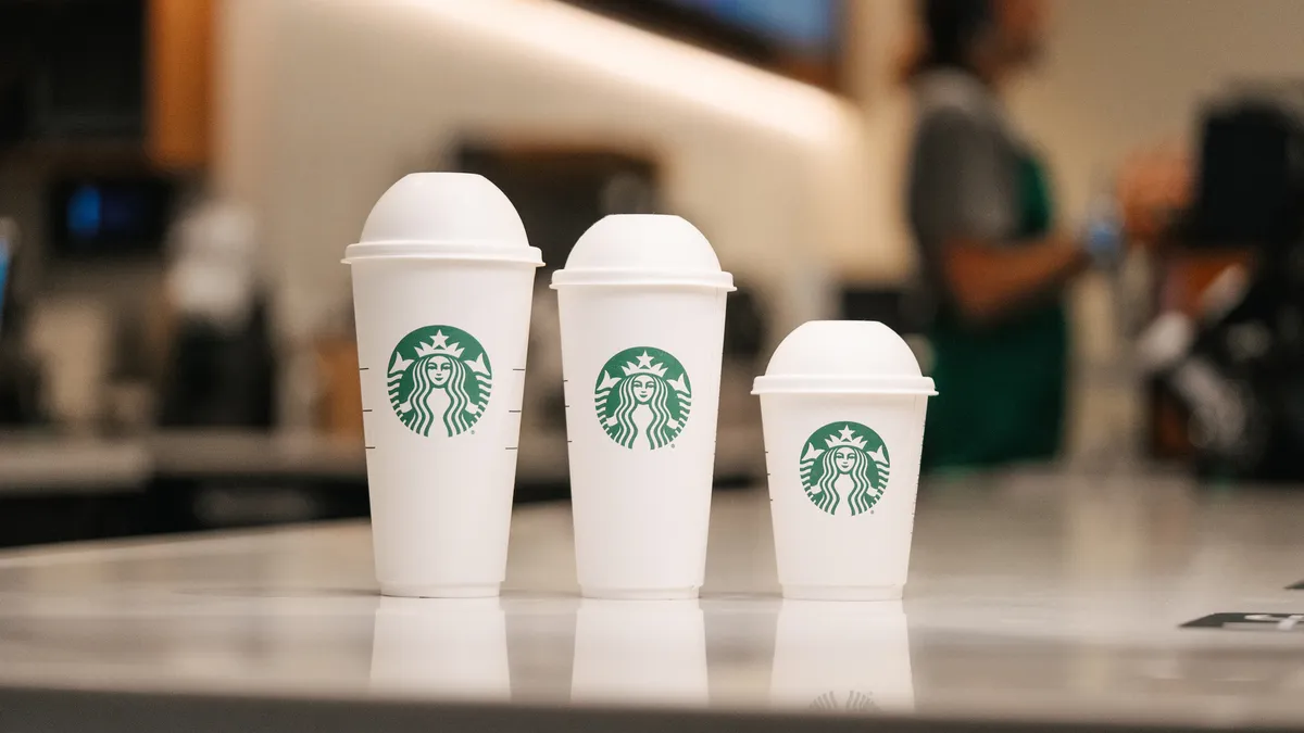 Three sizes of white fiber-based Starbucks cups with the company's green logo printed on them.