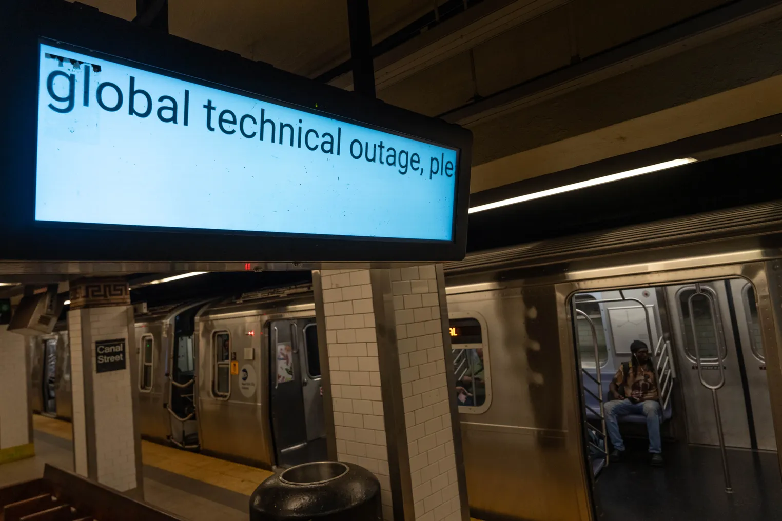 a screen hangs above a subway station, showing the words "global technical outage"