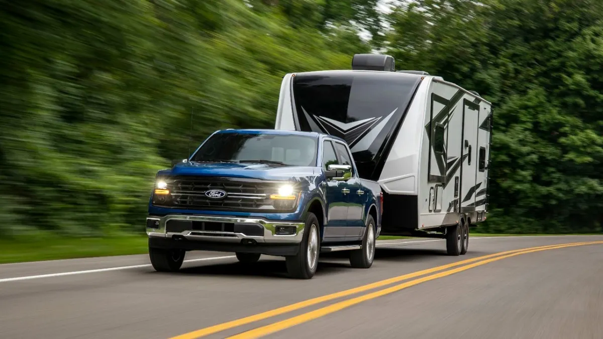 A blue 2024 Ford F-150 pickup driving on a highway while towing a camper.