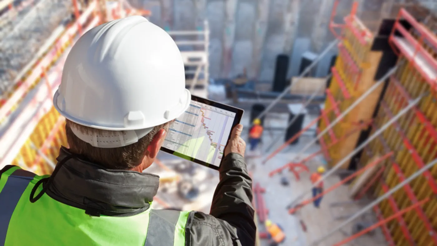 A construction worker with a tablet looks down at a jobsite below.