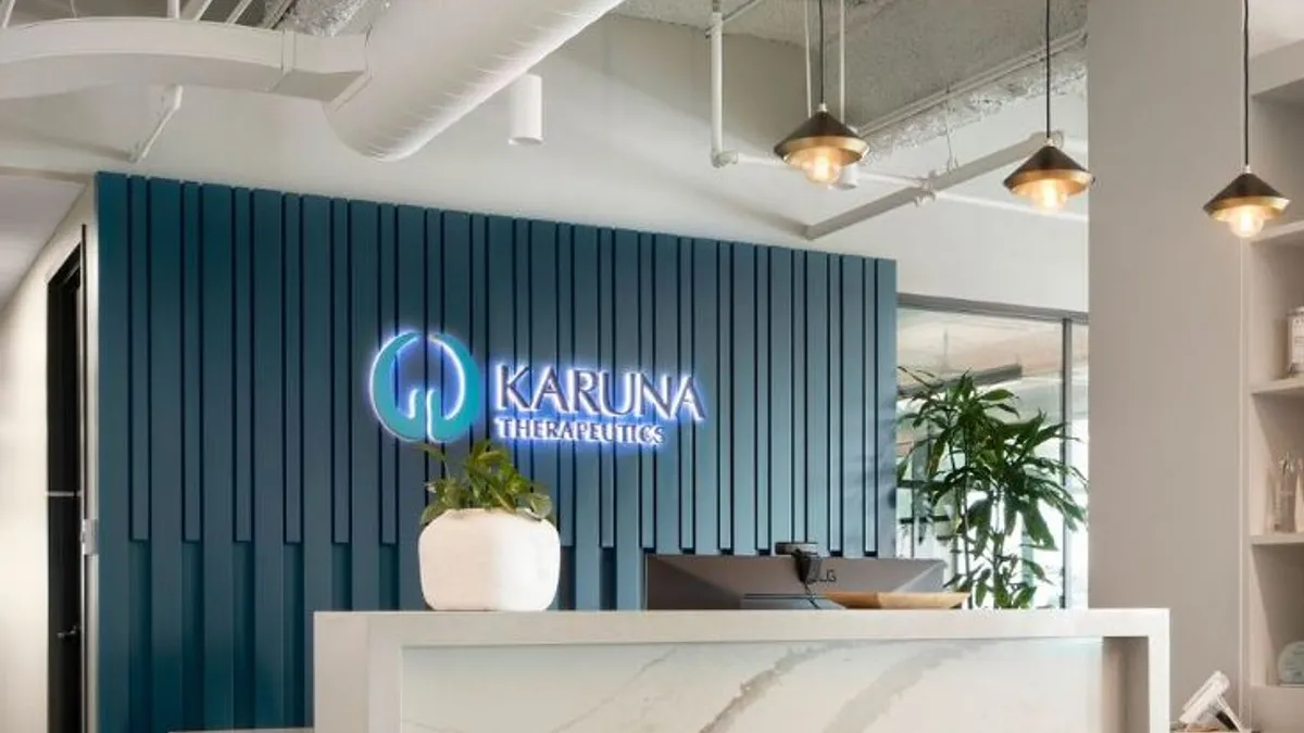 A backlit Karuna Therapeutics sign on a teal wall sits behind a white marble reception desk