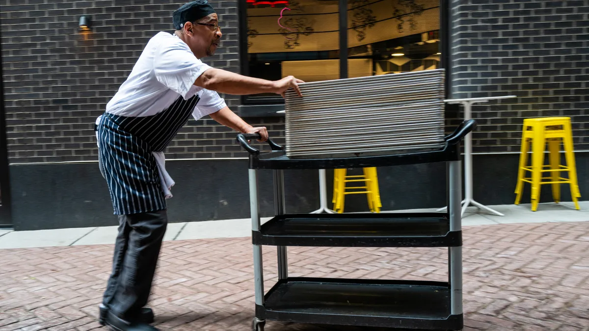 A restaurant employee pushes a cart down a city sidewalk.