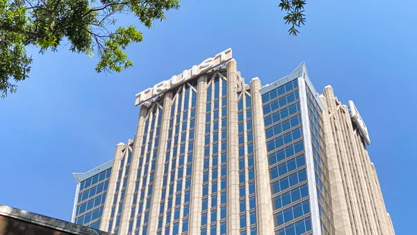 A sign that reads "Truist" sits atop a tall stone and glass office building.