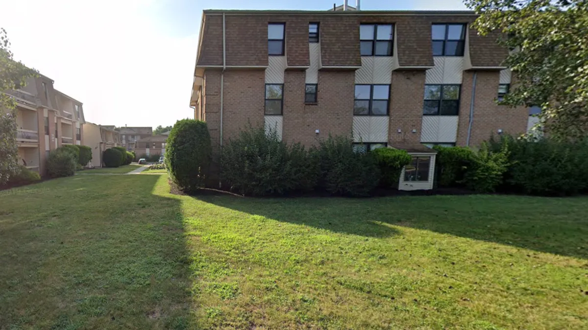 A three-story beige building surrounded by green grass.