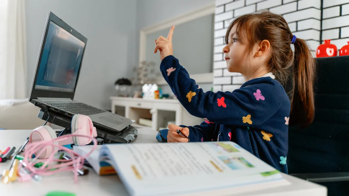 A young student video conferences with a teacher and classmates on the computer in a living room at home.